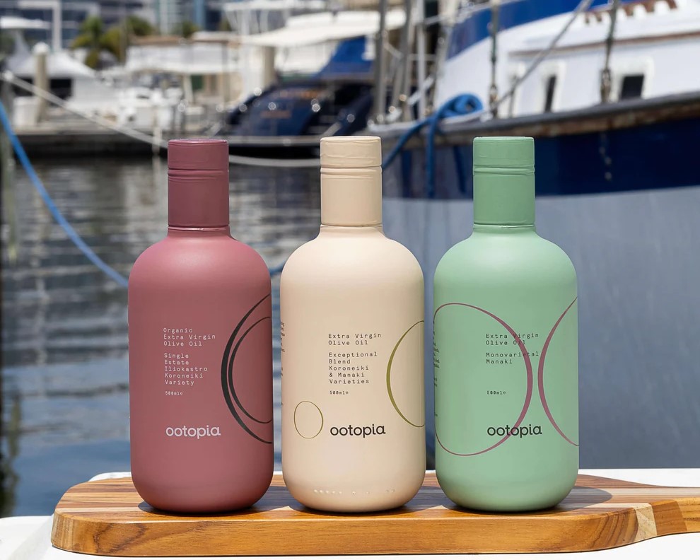 Tri fľaše extra panenského olivového oleja Ootopia na drevenej doske, v pozadí prístav.